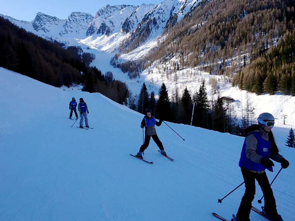 Skifahrende auf einer sonnigen Piste vor den Bergen.